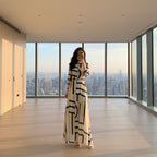 Woman in a long dress with geometric pattern standing in a room with a large teddy bear and abstract art on the wall.