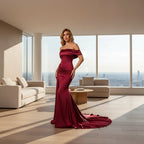 Woman in a burgundy off-shoulder gown posing against a dark background with a red couch.
