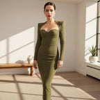 Woman in a green dress standing in an indoor setting with a mirror and flowers in the background.